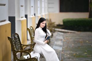 Elegant Vietnamese student in white Ao Dai reading, timeless beauty amidst classic architecture.-8