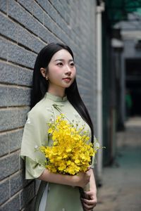 Graceful Vietnamese girl in green Ao Dai with yellow flowers at sacred pagoda-4